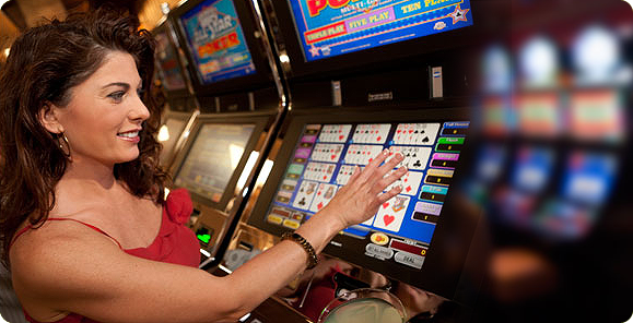 Симпатичная шатенка в красом платье касается рукой к монитору автомата с виде покером