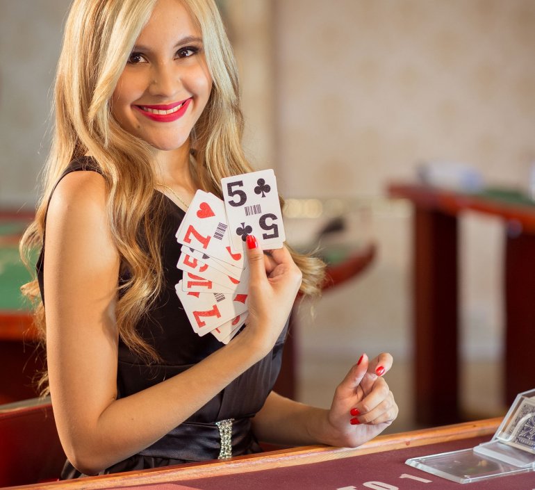 Симпатичная блондинка приветливо улыбается, демонстрируя карты для игры в баккара