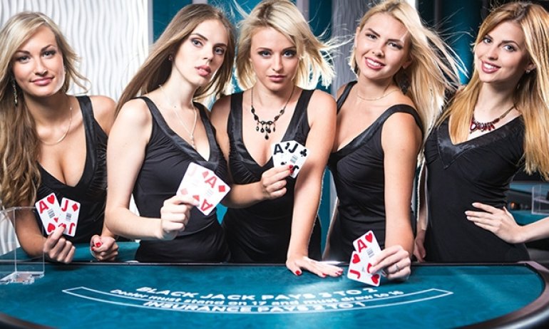 Пятеро блондинок в обтягивающих черных платьях с откровенными декольте позируют с картами в руках у стола для игры в блэкджек