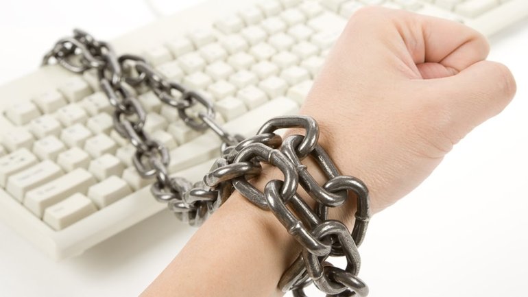 Мужская рука прикованная крупной цепью к клавиатуре компьютера