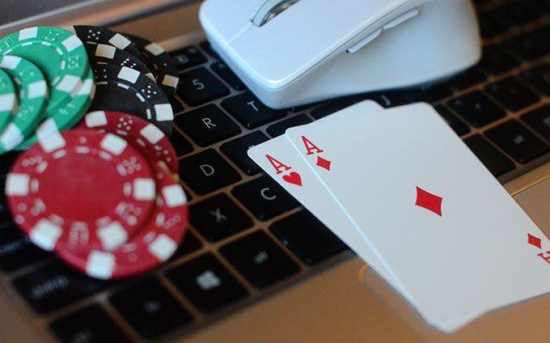 На клавиатуре ноутбука леждат карты, мышка и фишки казино